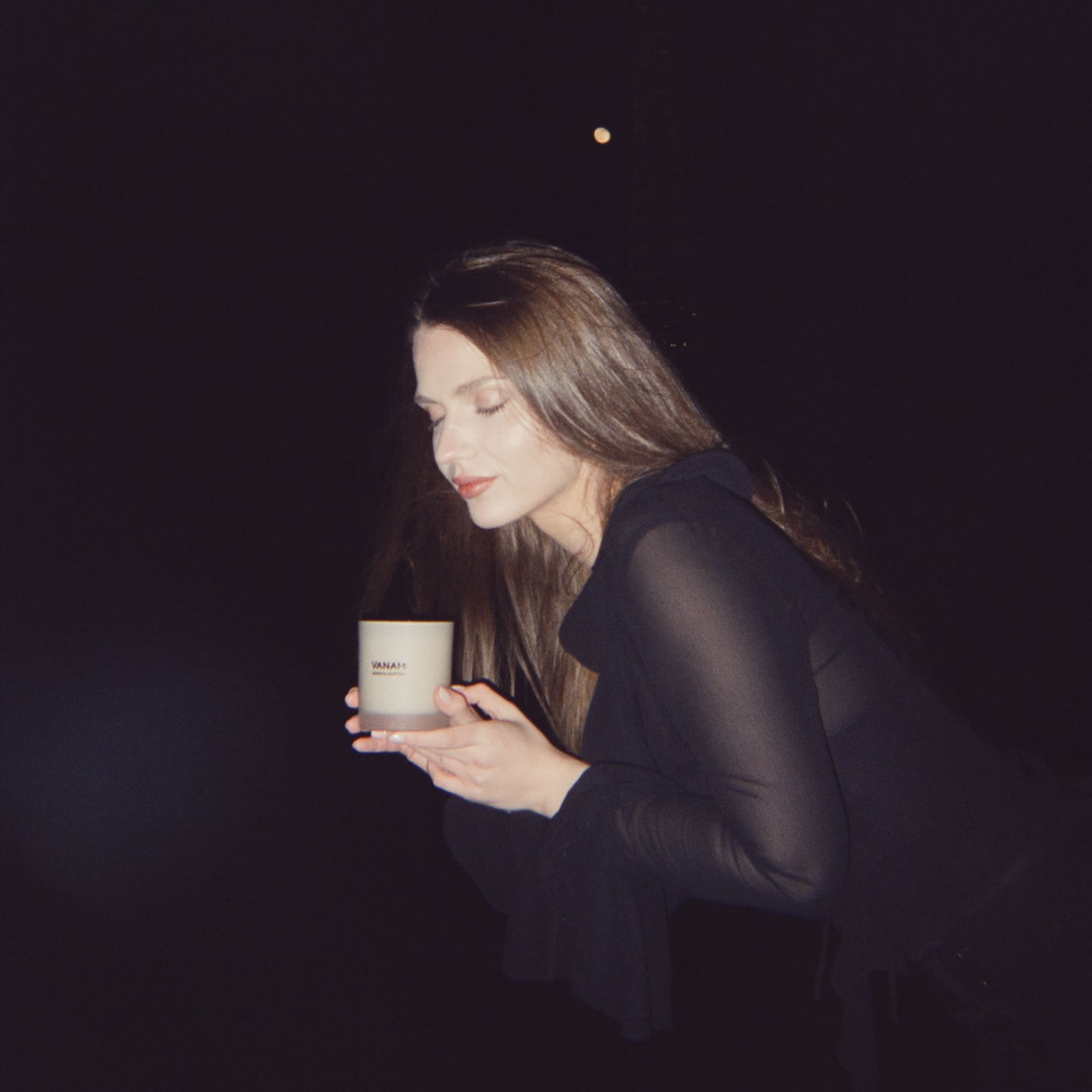 Woman holding a Vanam candle against a dark background