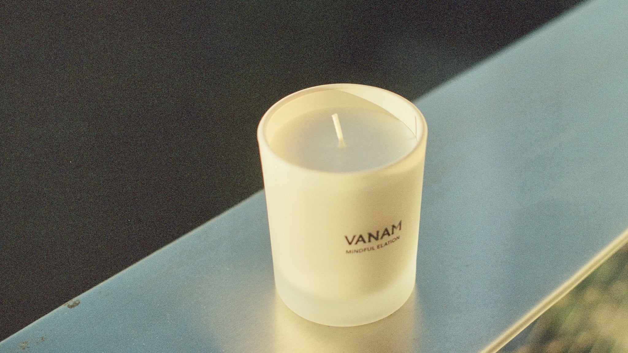 Vanam Mindful Elation Beeswax Candle on a reflective surface with a dark background
