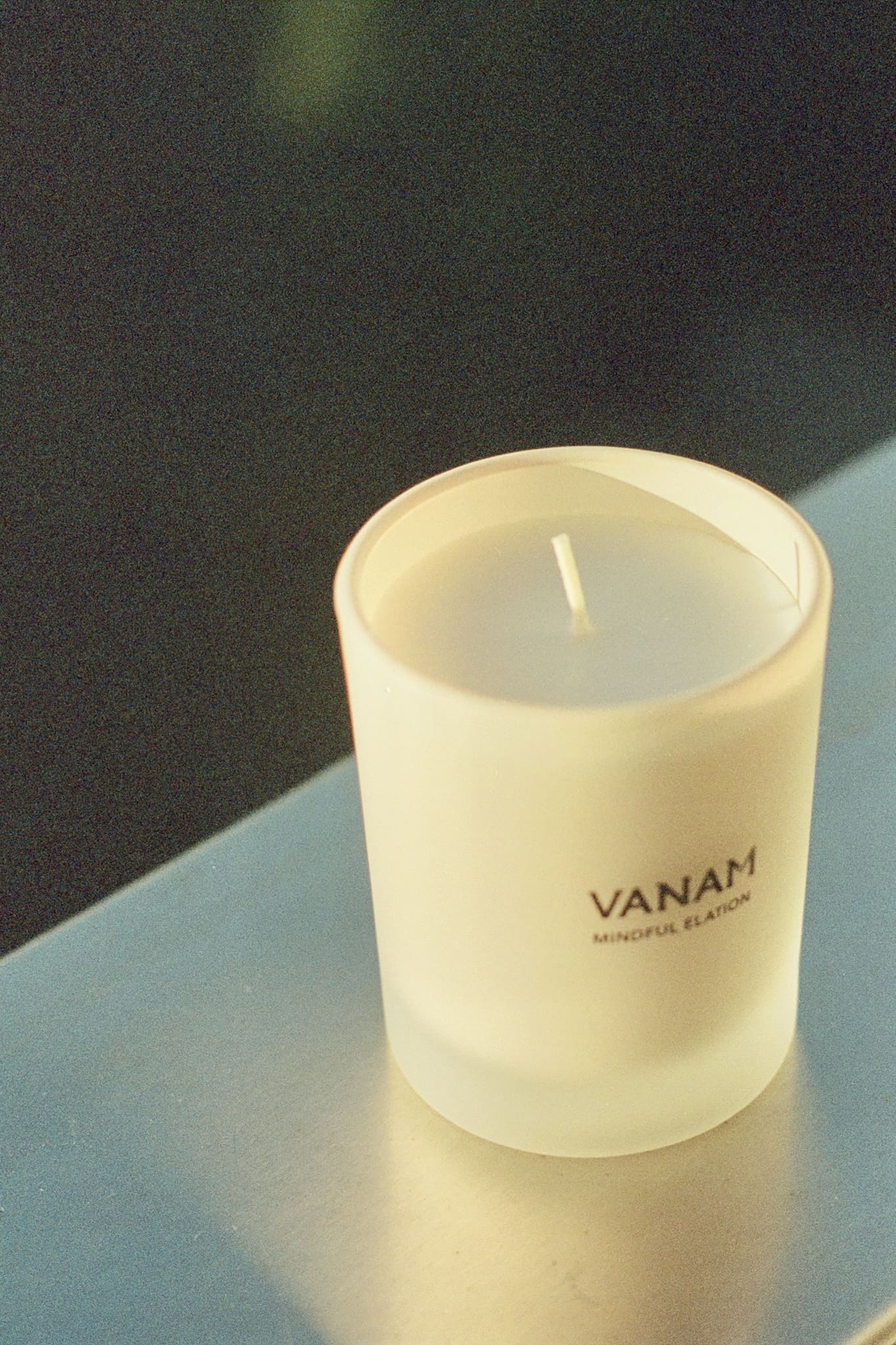 Vanam Mindful Elation Beeswax Candle on a reflective surface with a dark background